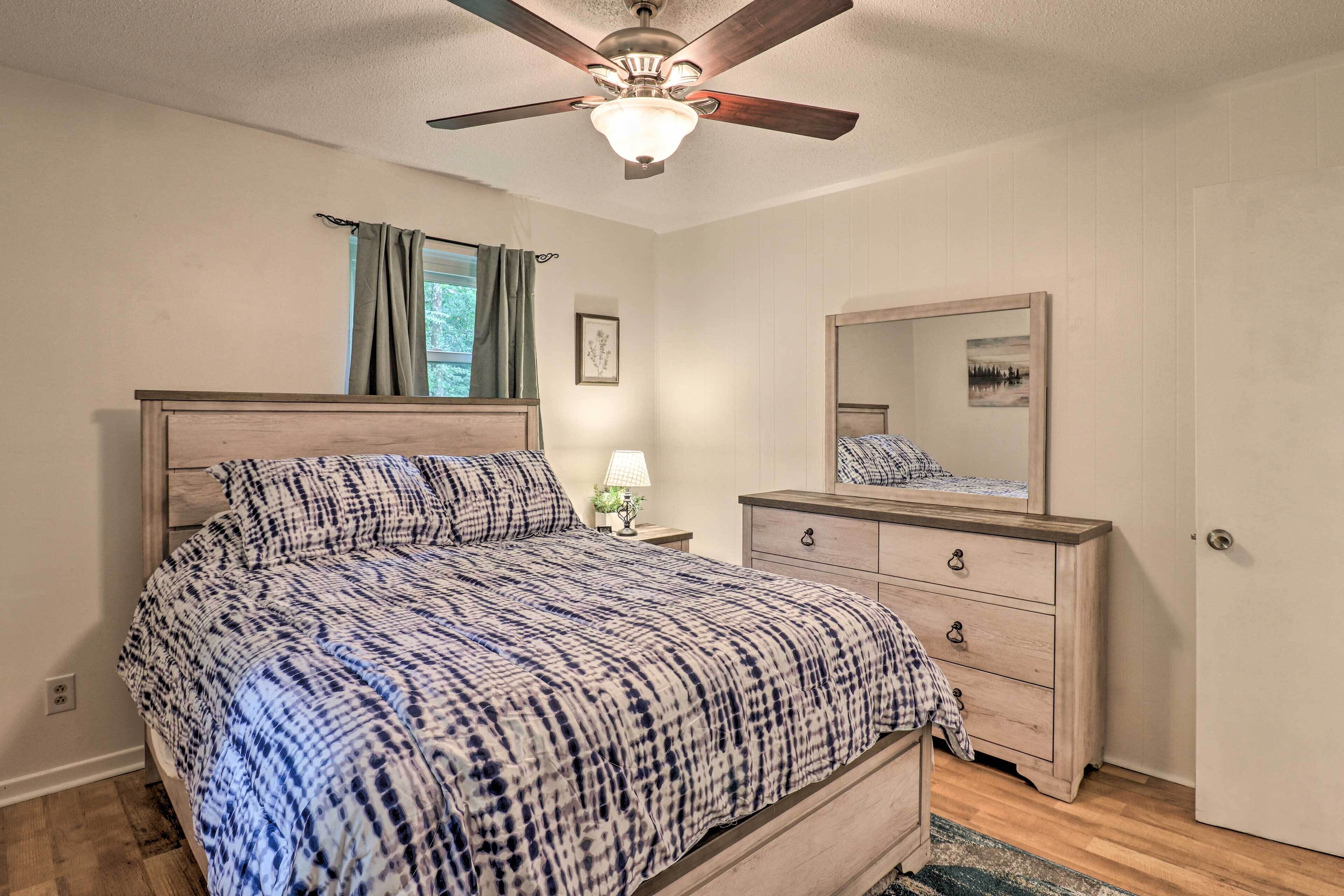 A bedroom with a bed, a dresser, a ceiling fan, a window with curtains, and a mirror.