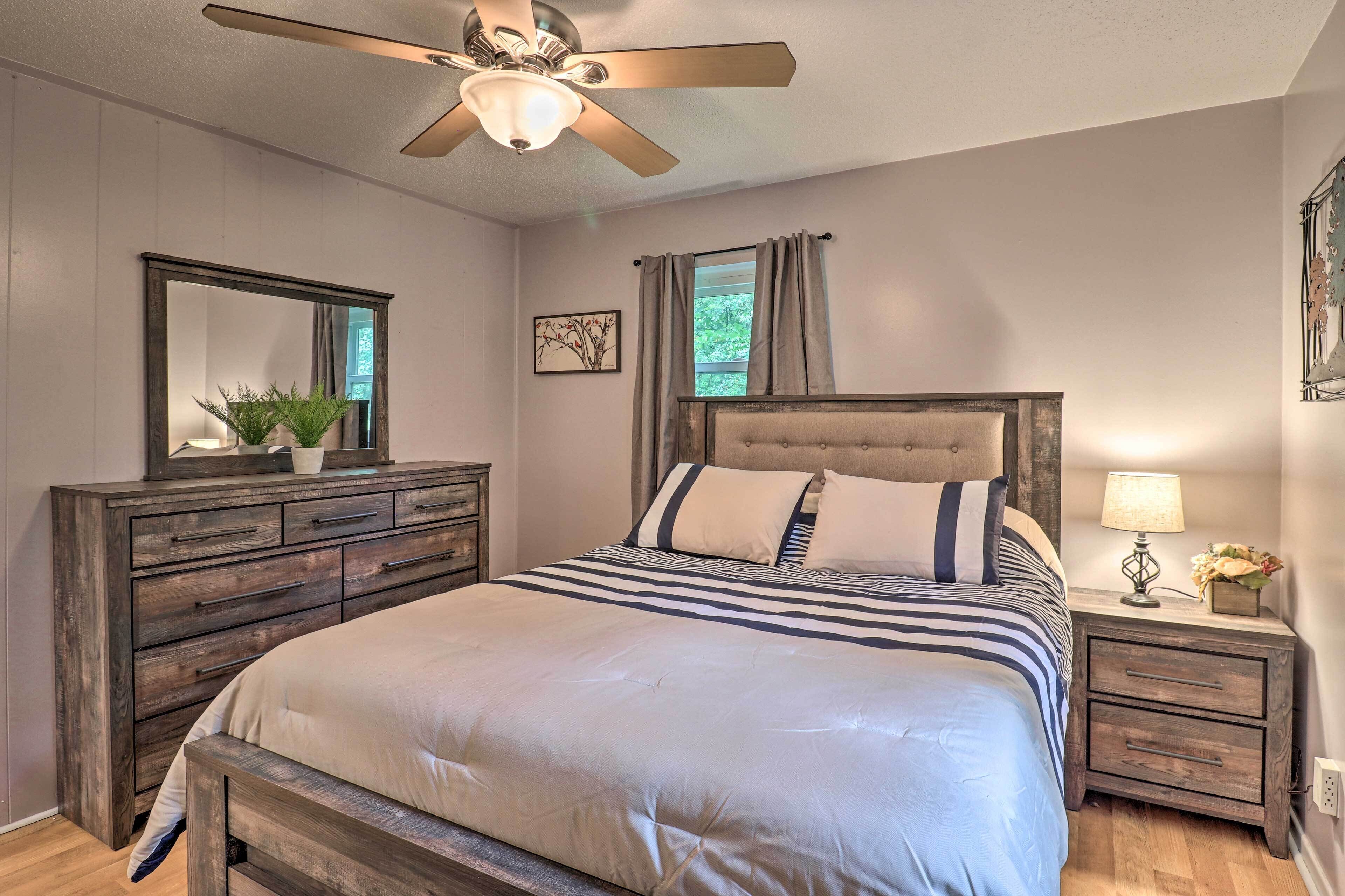 A bedroom with a bed, a dresser, a nightstand, a ceiling fan, and a window with curtains.