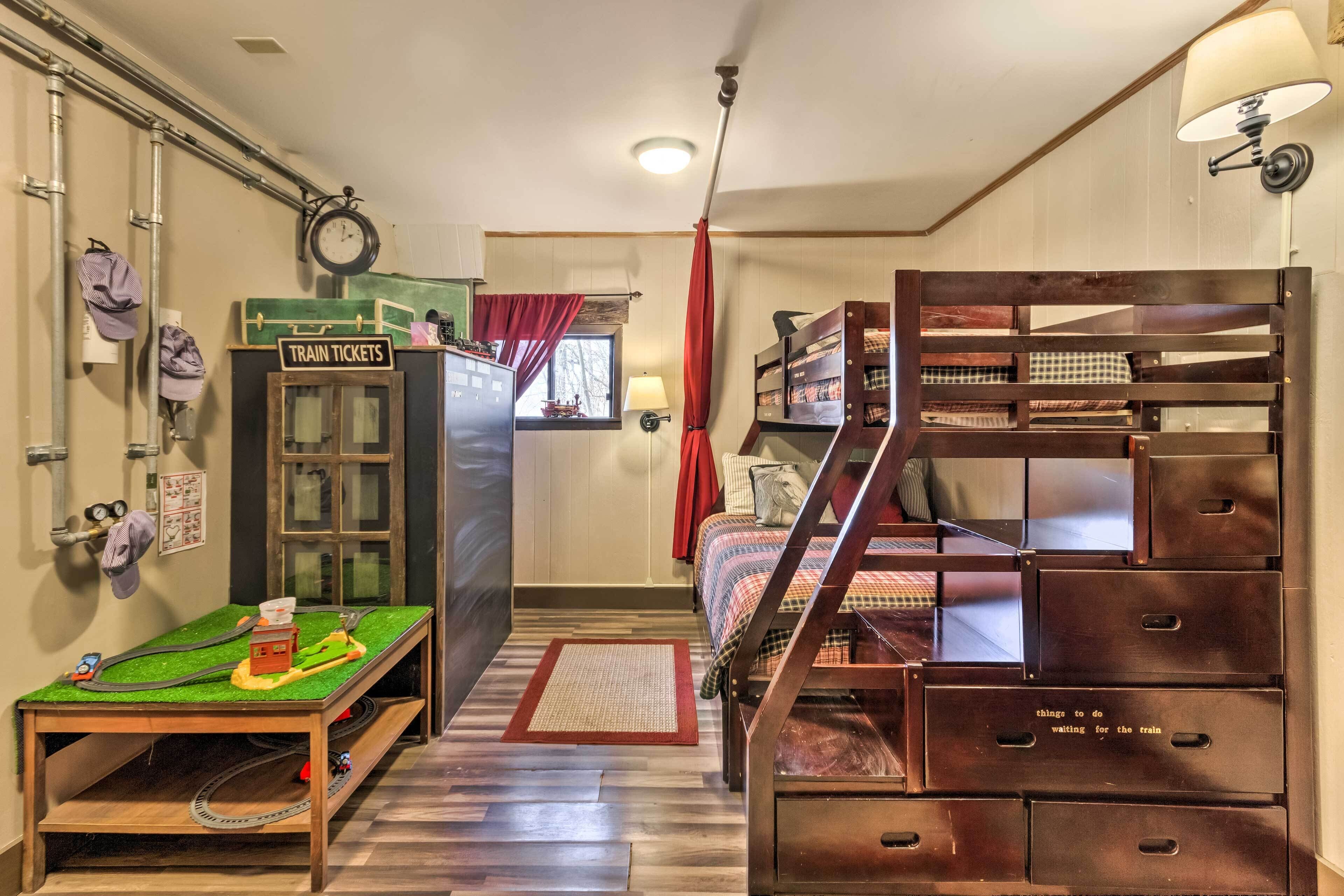 A room with a train-themed setup including a model train set, a 'Train Tickets' sign, and a ladder leading to a bunk bed.