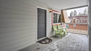 Eine Veranda mit einer grauen Tür, einem Fenster mit rotem Rahmen und zwei grünen Adirondack-Stühlen.