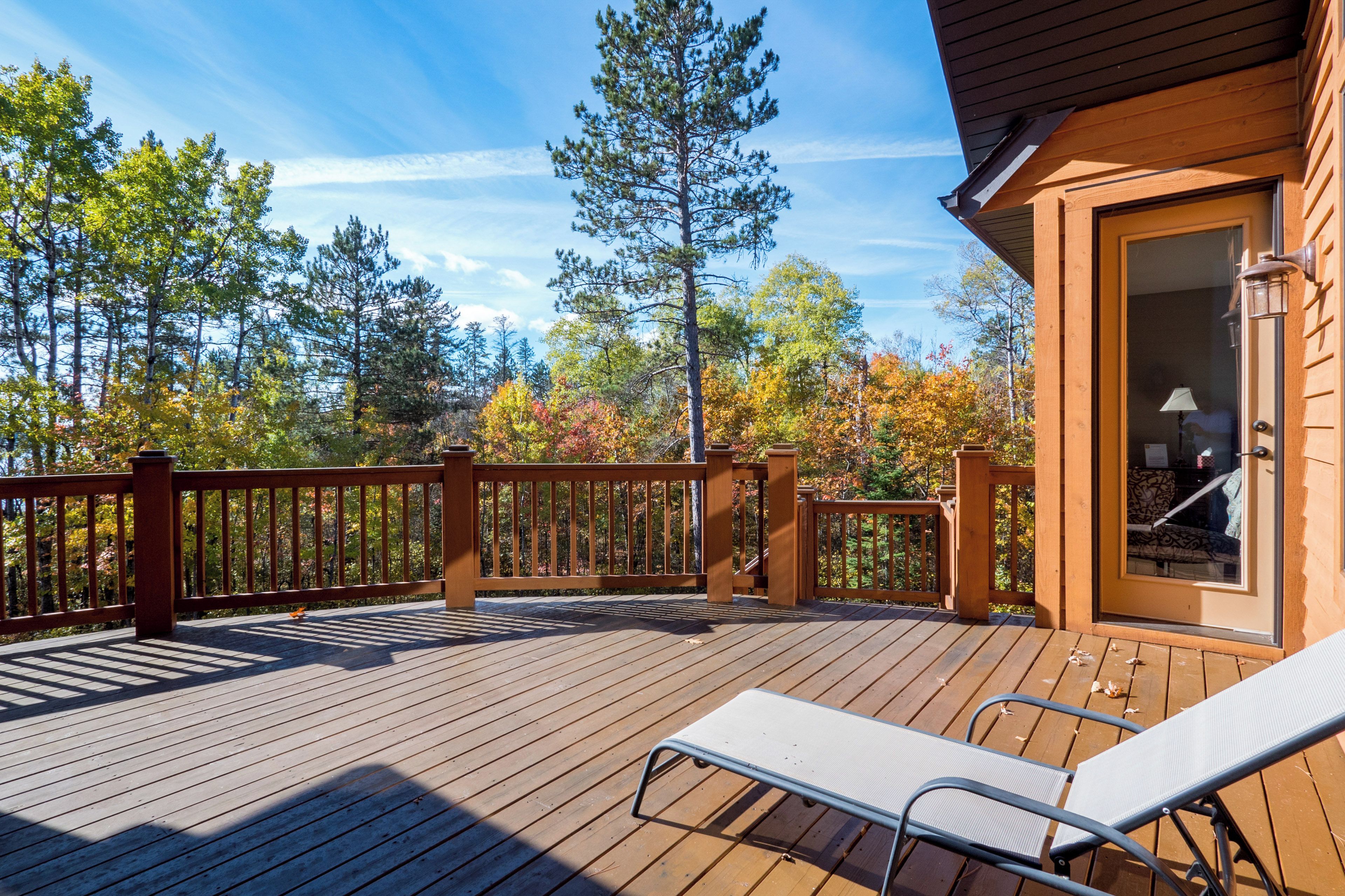 A wooden deck with a railing, a lounge chair, and a door with a window.