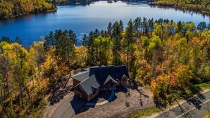 A lodge with a stone exterior and multiple roofs, surrounded by a forest with autumn foliage, near a large lake. - Lakefront Giants Ridge Retreat Near Ski & Golf! (Aurora)