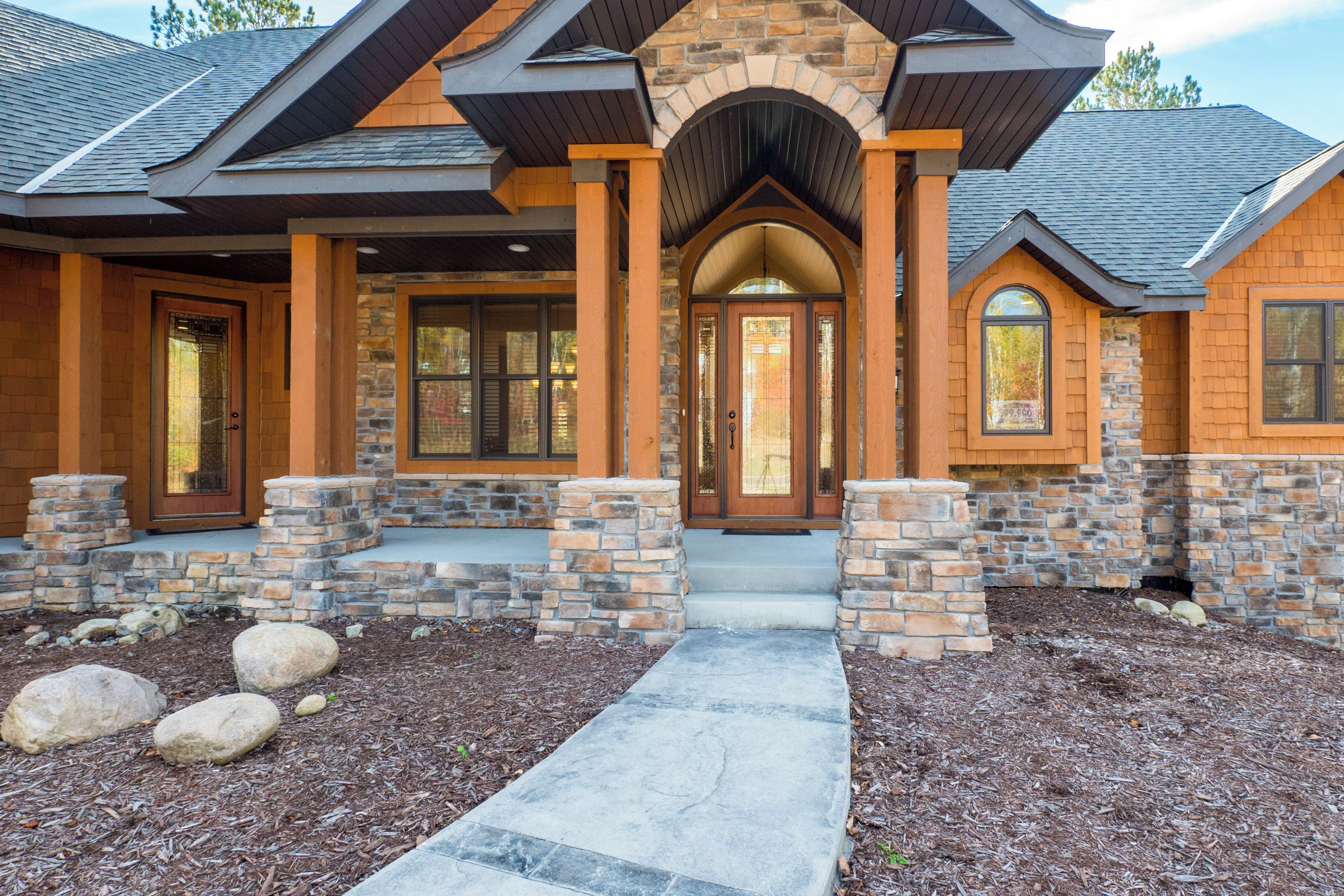 A modern house with a stone facade, a central entrance with a glass door, and a stone pathway leading to the front door.