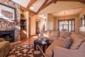 A spacious living room with a stone fireplace, wooden beams, a large sofa, and a dining area with a chandelier. - Lakefront Retreat at Giants Ridge: Golf, Hike, Ski (Aurora)