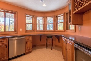 A kitchen with wooden cabinets, a stainless steel dishwasher, and a bar stool. - Lakefront Retreat at Giants Ridge: Golf, Hike, Ski (Aurora)