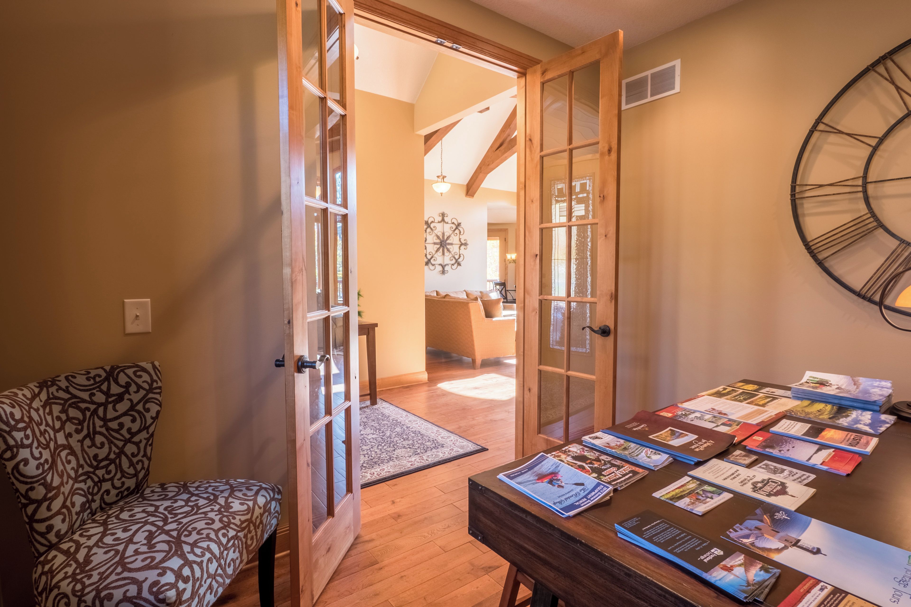 A room with a patterned chair, a table with brochures, and a wooden door leading to another room.