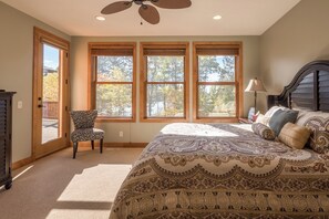 A bedroom with a large bed, a chair, a ceiling fan, and a view of trees through the windows. - Lakefront Retreat at Giants Ridge: Golf, Hike, Ski (Aurora)
