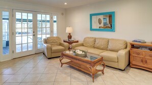 A living room with a beige sofa, a glass-top coffee table, a wicker side table, and a blue-framed mirror on the wall. - Beach Retreat in Jacksonville: Pet/family-friendly (Jacksonville Beach)