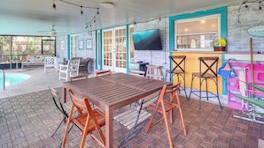 An outdoor patio area with a wooden table and chairs, a pool, and a bar area with stools. - Beach Retreat in Jacksonville: Pet/family-friendly (Jacksonville Beach)