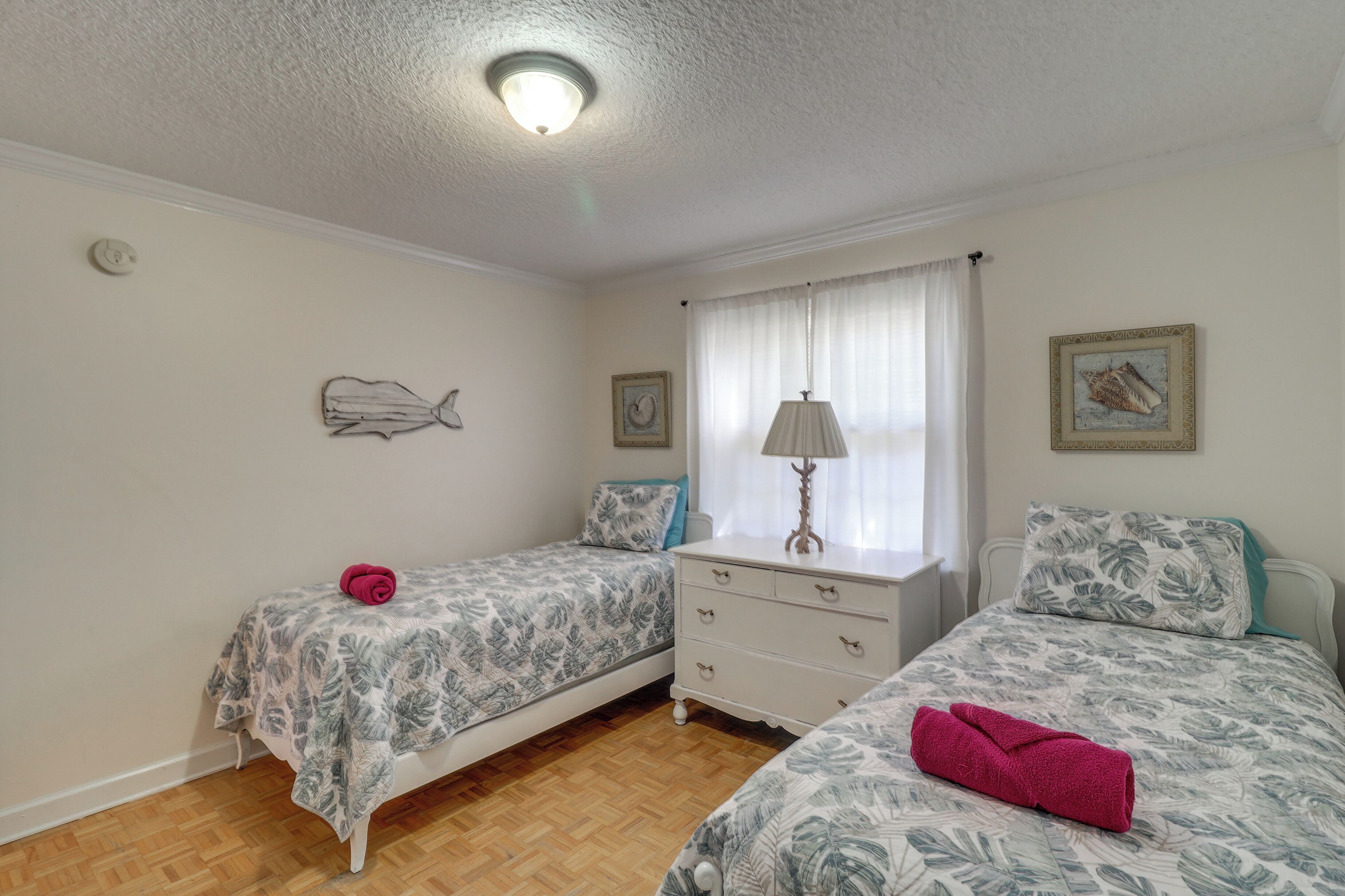 A bedroom with two beds, a dresser, a lamp, and artwork on the walls.