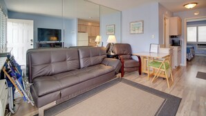 A living room with a brown leather sofa, a dining table with a green cushion, and a kitchen in the background. - First-floor Brigantine Condo: Steps to Ocean! (Brigantine)