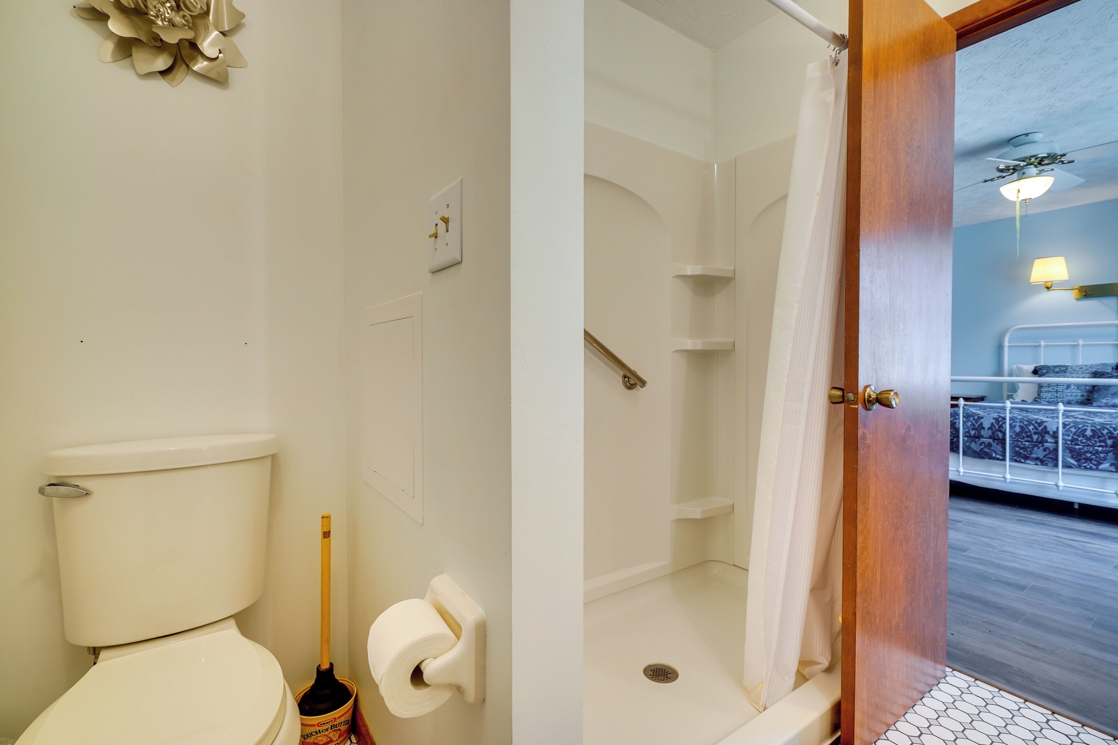A bathroom with a toilet, a shower, and a door leading to a bedroom.