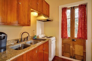 A kitchen with wooden cabinets, a stove, a sink, and a window with red curtains.