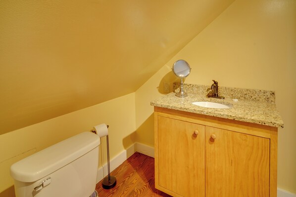 A bathroom with a toilet, sink, vanity, and mirror.