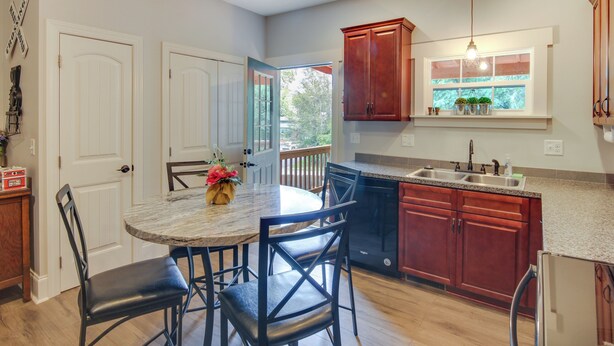 A kitchen with a dining table, chairs, wooden cabinets, a window with plants, and a built-in oven.