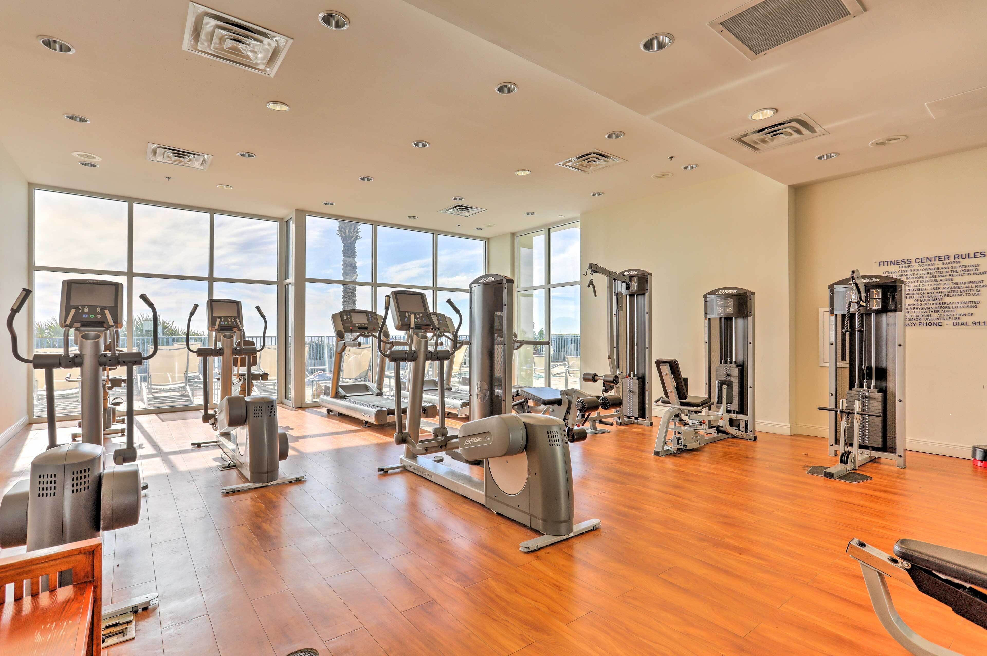 A spacious gym with various exercise machines, large windows, and a wooden floor.