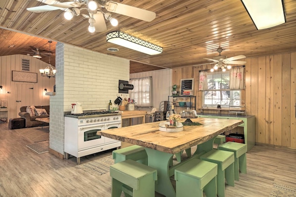 Uma cozinha rústica com mesa de madeira, banquetas verdes e fogão branco.