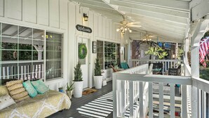 Ein überdachter Balkon mit weißer Reling, einer Couch mit gemusterten Kissen und einem 'Welcome'-Schild.