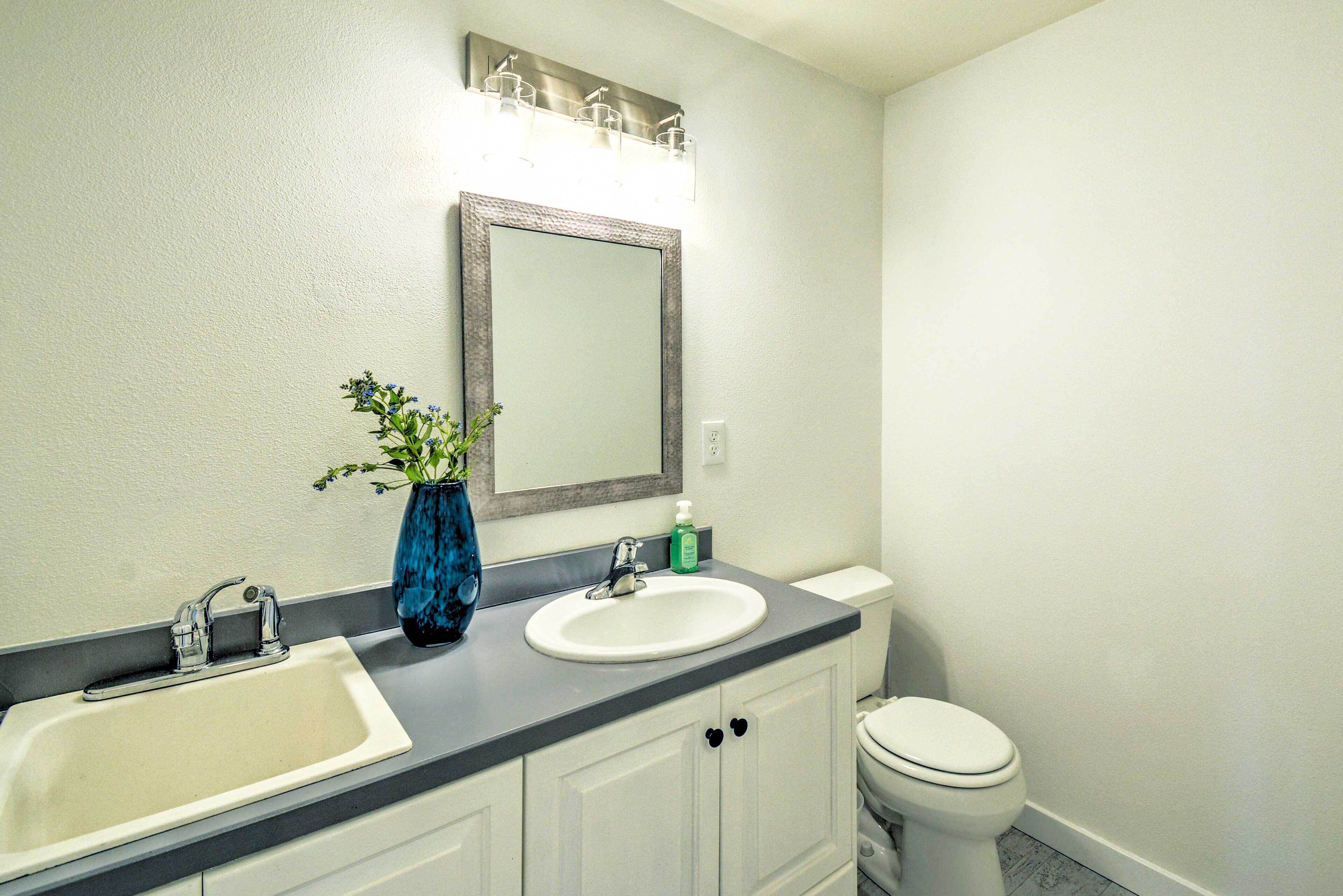 A bathroom with a double sink, a mirror, a toilet, and a vase with flowers.