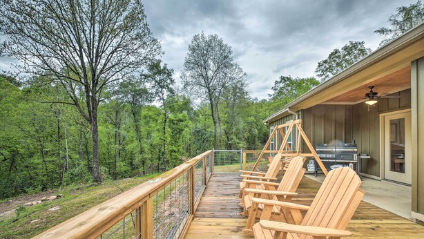 Une terrasse en bois avec des fauteuils Adirondack, un barbecue et une vue sur une zone boisée.