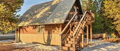 Une cabane en bois avec un toit en métal, un escalier menant à un porche et un espace abrité avec un banc en bois.