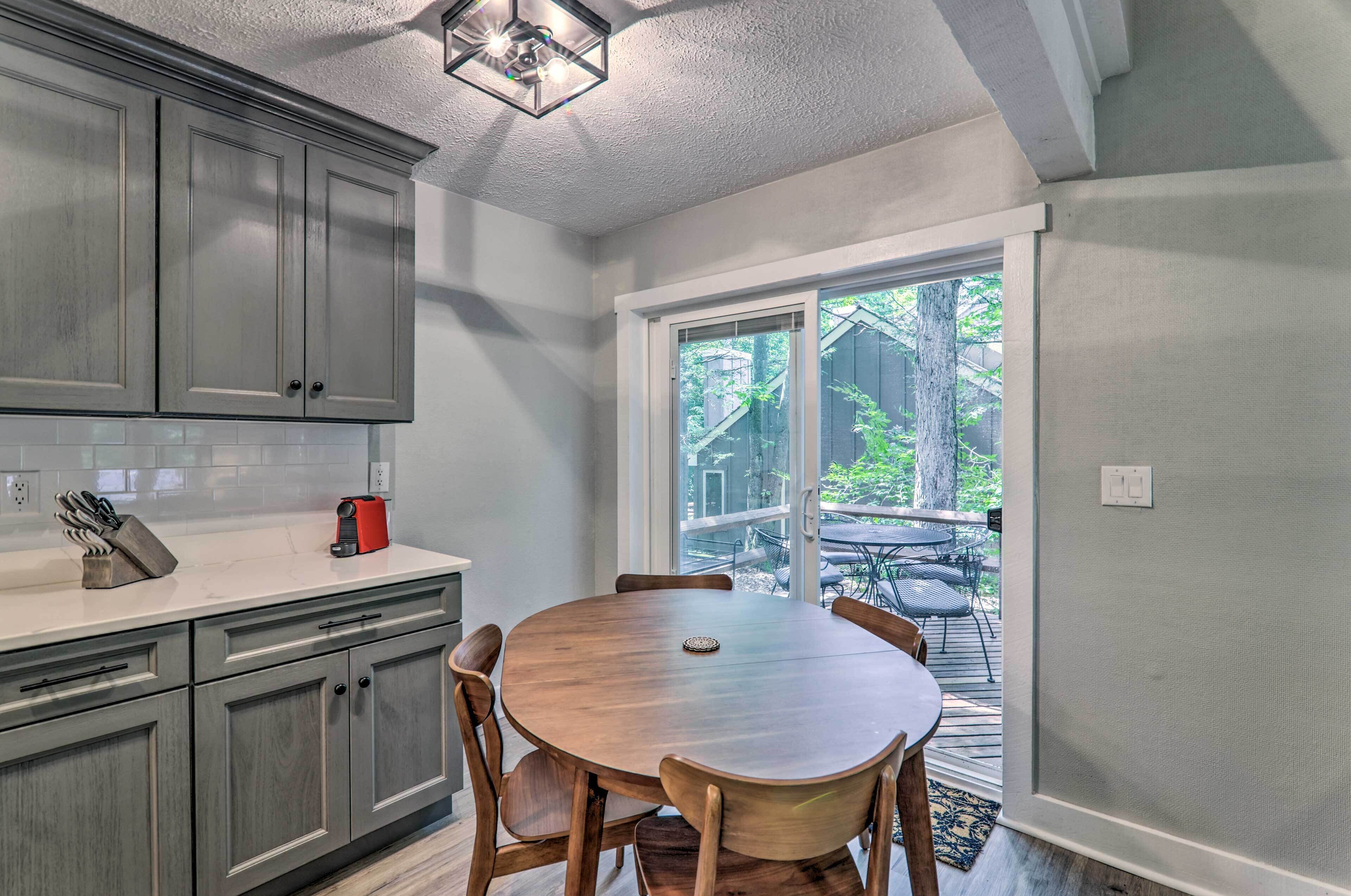 A kitchen with grey cabinets, a round wooden table, and a window leading to an outdoor area.