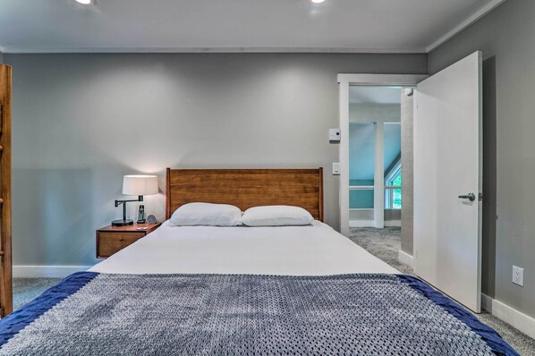 A bedroom with a wooden headboard, a bed with white linens, a bedside table with a lamp, and a blue and white patterned throw. - Unwind Fireside & Walk to Slopes! Poconos Getaway (White Haven)