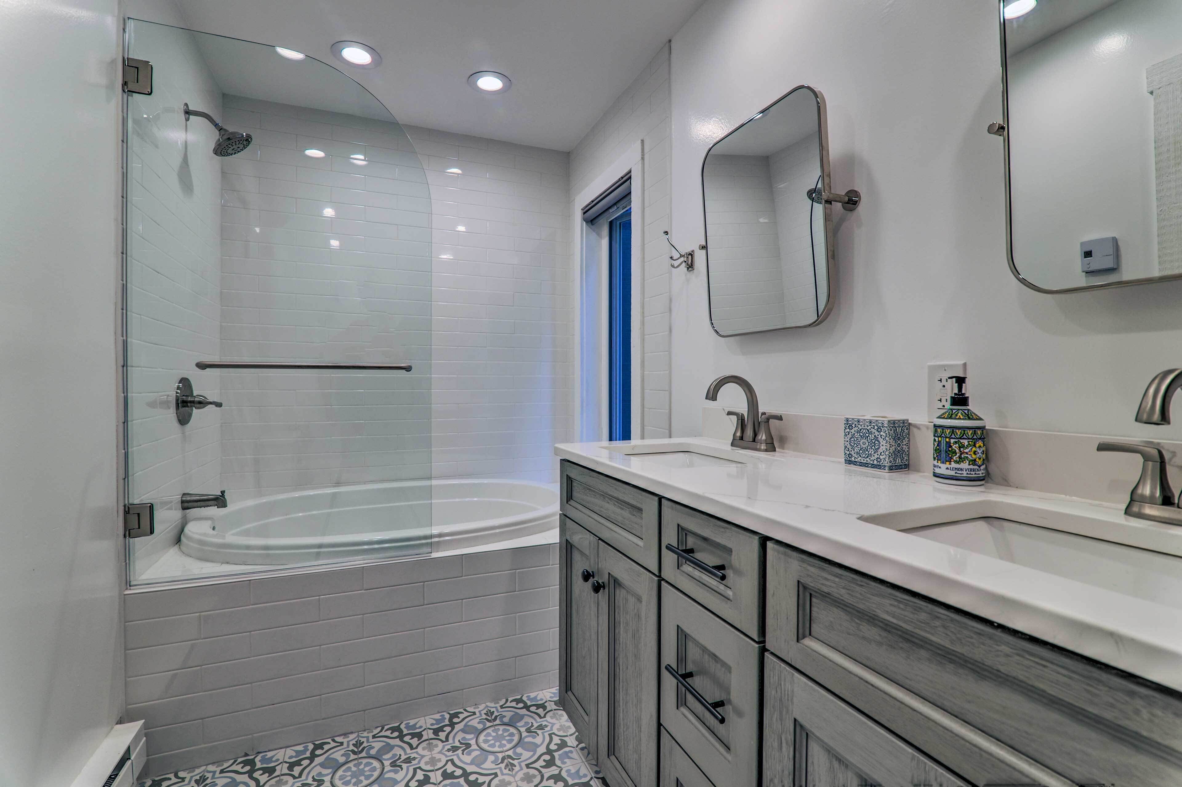 A modern bathroom with a glass-enclosed shower, a freestanding bathtub, and a vanity with a sink and mirror.