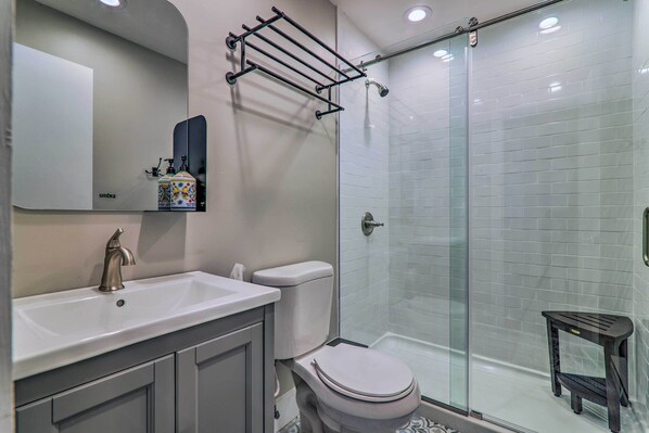 Een moderne badkamer met een wit wastafelmeubel, toilet, glazen douchecabine en een klein zwart krukje.