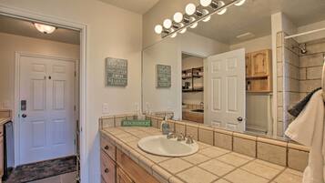 A bathroom with a white sink, vanity, and a large mirror with lights. There are motivational signs on the wall and a towel rack.