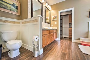 Een badkamer met toilet, wastafel en spiegel. Er is een houten kastje en een lijst met een foto aan de muur.