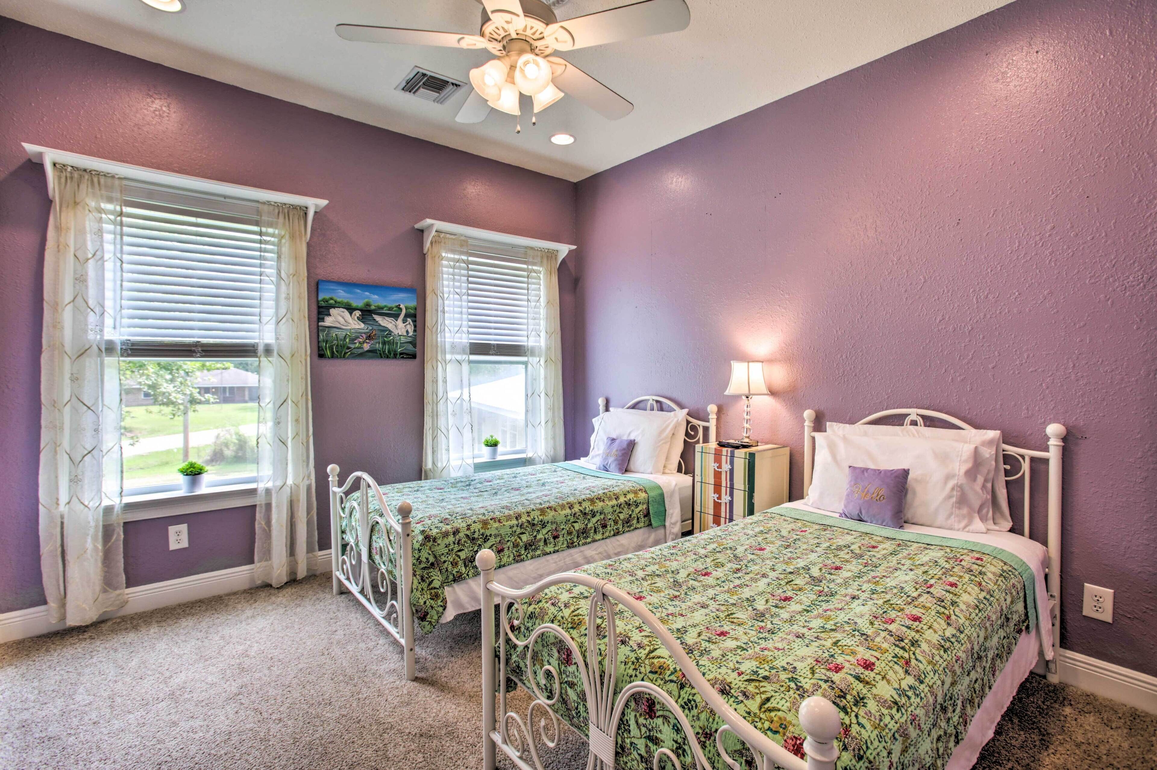 A bedroom with two beds, purple walls, and a ceiling fan.
