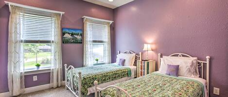 A bedroom with two beds, purple walls, and a ceiling fan.