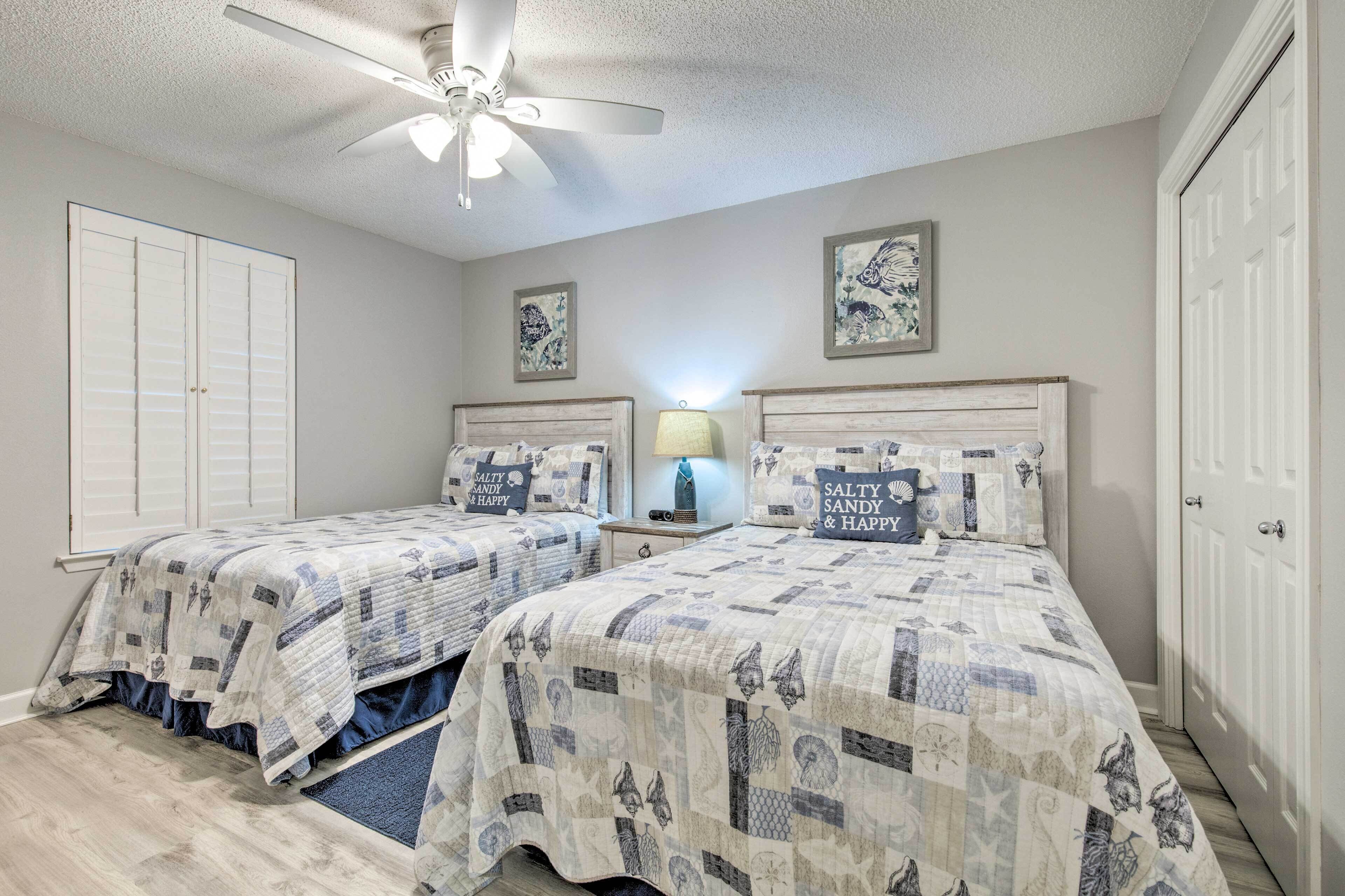 A bedroom with two beds, a ceiling fan, and artwork on the walls.