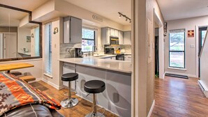 A modern kitchen with a central island, bar stools, and a dining area with a bench. - 2 Blocks to Skiing & Mtb: Angel Fire Condo (Angel Fire)
