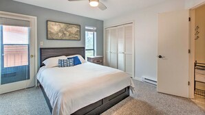 A bedroom with a bed, a ceiling fan, a window with blinds, a door, and a wall-mounted artwork. - 2 Blocks to Skiing & Mtb: Angel Fire Condo (Angel Fire)