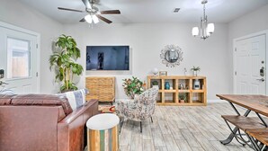 A spacious living room with a brown leather sofa, a patterned armchair, a wooden dining table, and a ceiling fan.