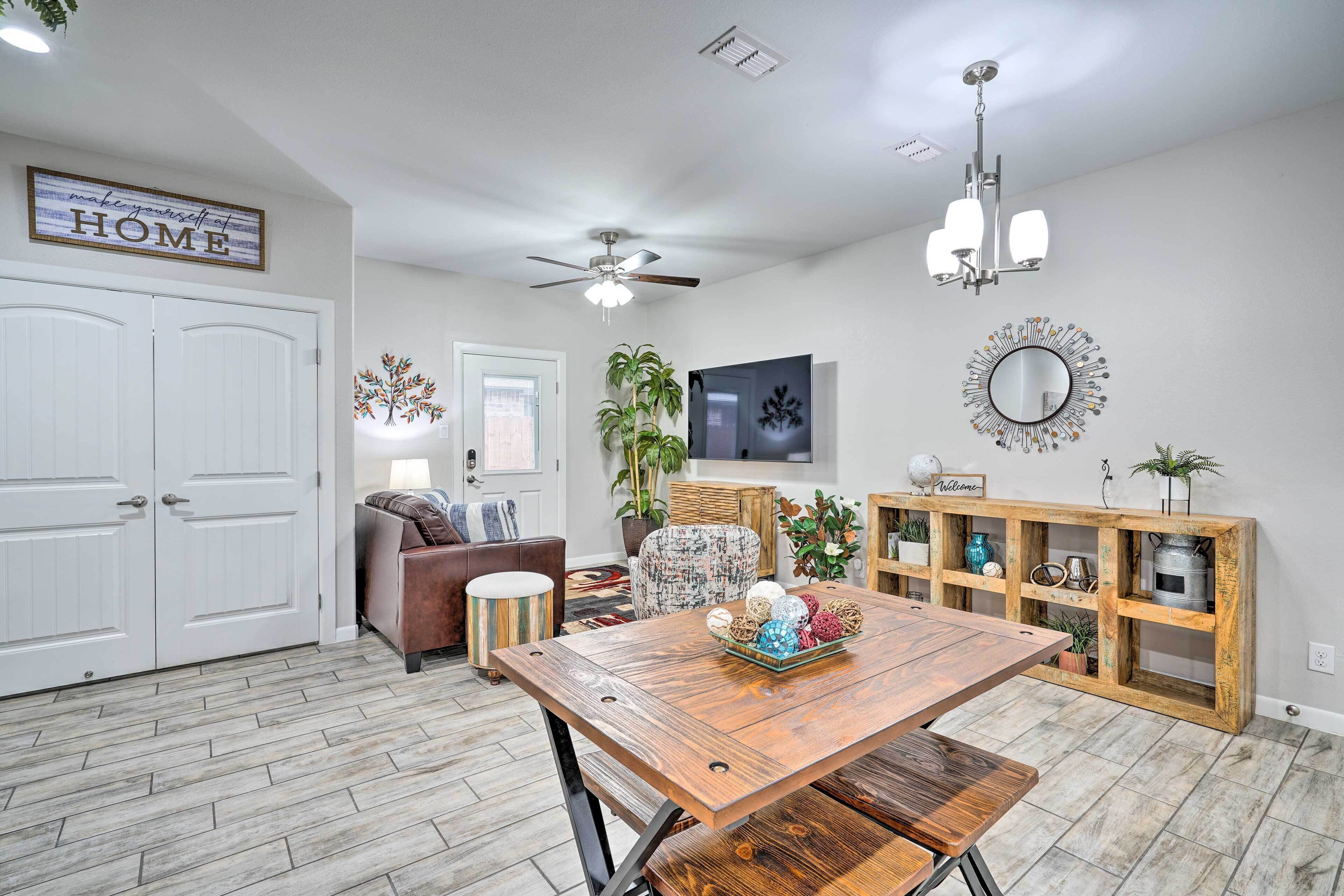 A living room with a wooden dining table, a ceiling fan, a TV, and a decorative mirror.