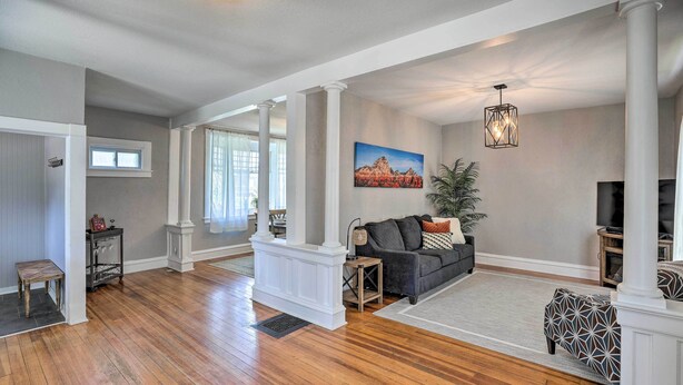 A spacious living room with hardwood floors, a gray sofa, a patterned ottoman, and a painting on the wall.