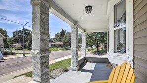 A porch with stone columns, a yellow Adirondack chair, and a view of a residential street.