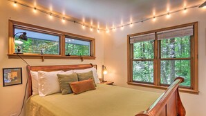 Ein Schlafzimmer mit einem Bett, zwei Fenstern mit Jalousien, Lichterketten und einem Nachttisch mit Lampe.