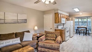 A cozy living room with a sofa, a patterned armchair, a coffee table, and a sign that reads "be our guest". There is a kitchen area with a refrigerator, stove, and dining table. - Cozy Ruston Townhome < 1 Mi to Louisiana Tech (Ruston)