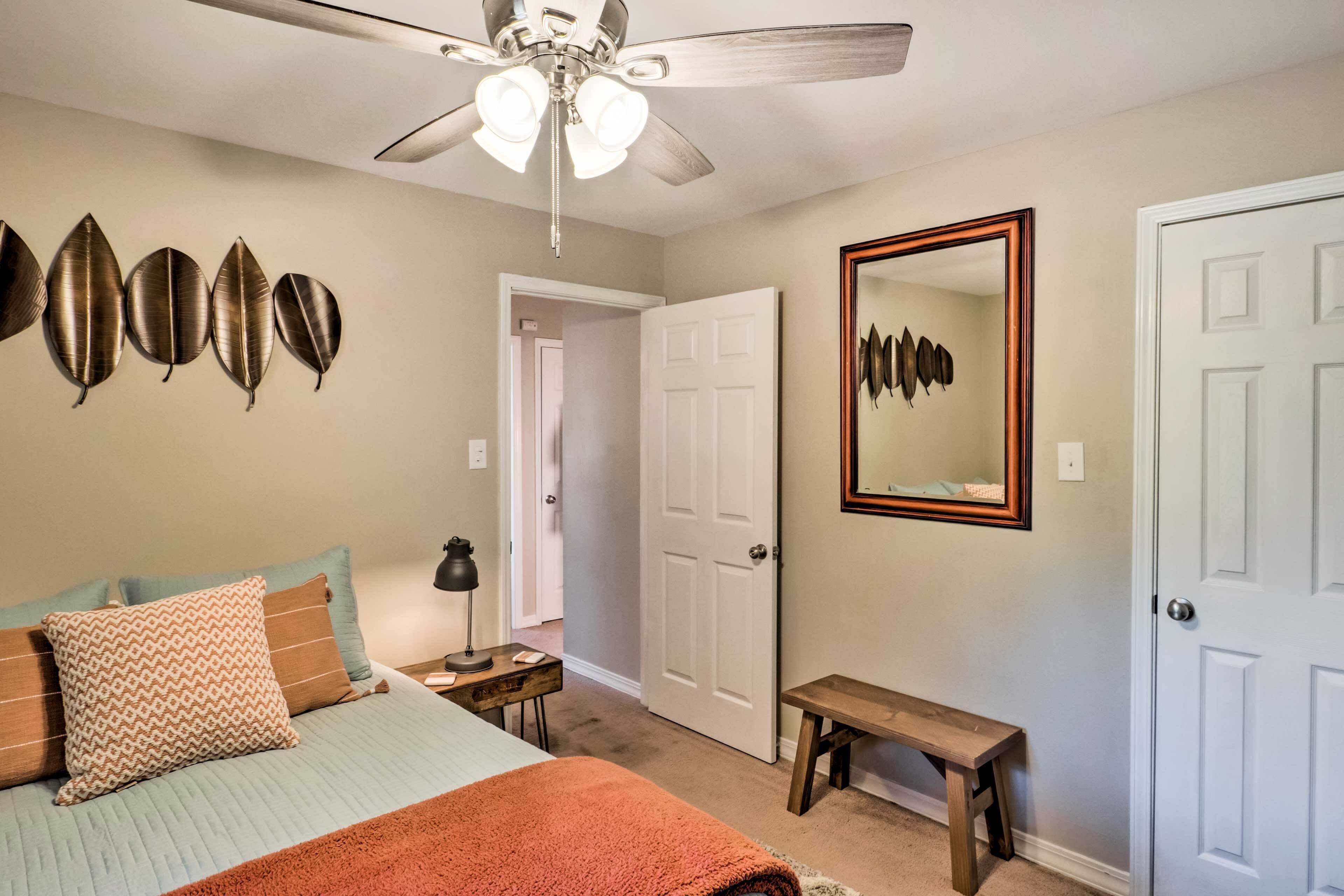 A bedroom with a bed, a ceiling fan, a wall-mounted mirror, and a door.