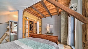 A bedroom with a wooden ceiling, a bed with a quilt, a stone pillar, and a window with curtains. - Country Escape w/ Fire Pit Near French Creek! (Cambridge Springs)