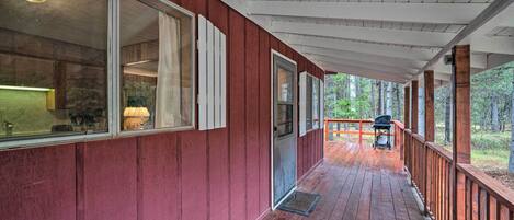 Une terrasse en bois couverte, avec une façade rouge, une porte-fenêtre coulissante et une vue sur la forêt.