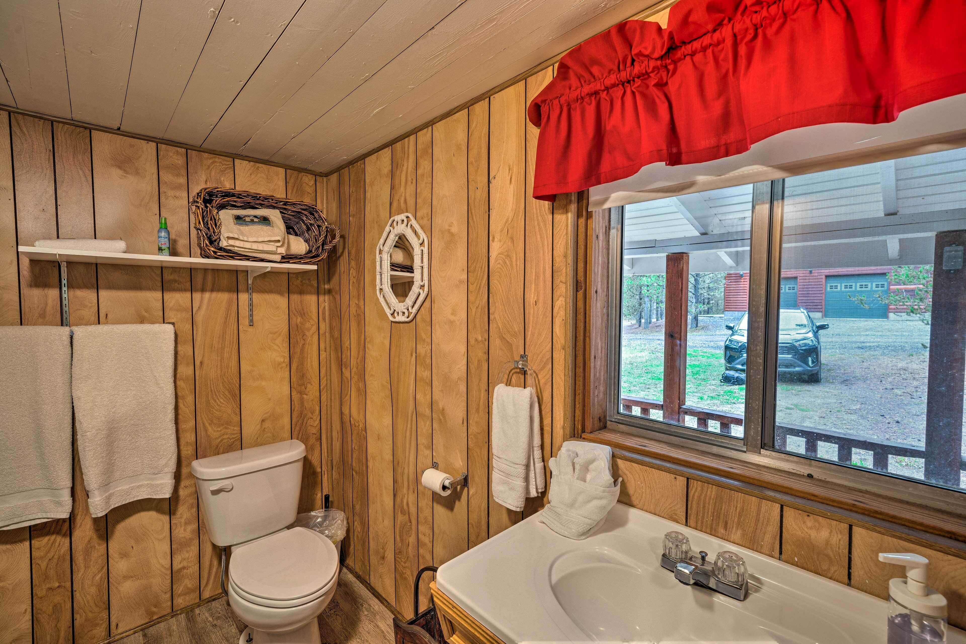 Un baño con paneles de madera, un inodoro, una bañera blanca con una cortina roja y una ventana con vistas a un estacionamiento.