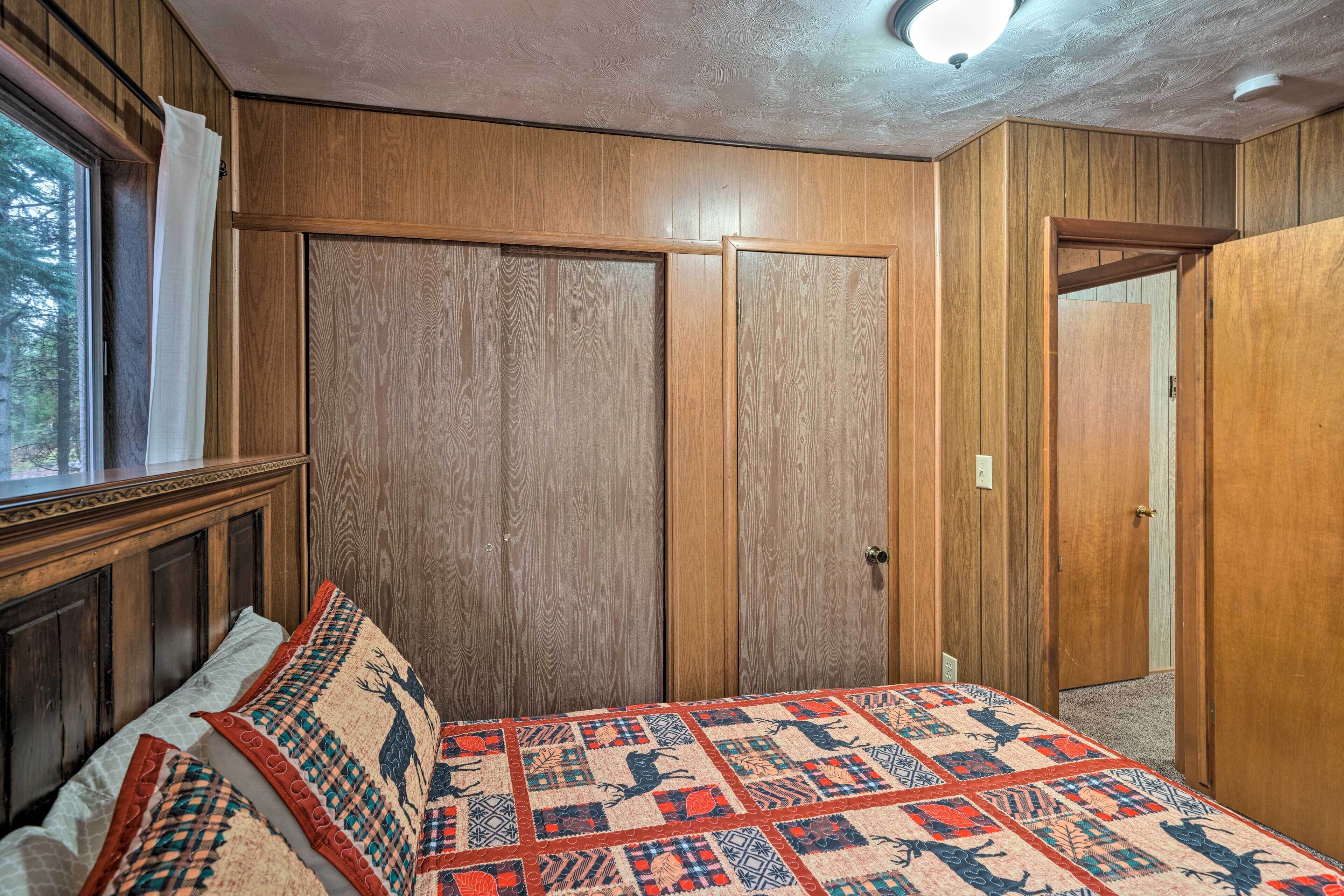 Une chambre avec des murs recouverts de panneaux de bois, un lit avec une literie à motifs et une fenêtre avec des rideaux.