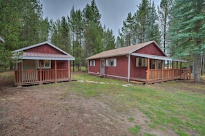 Two cabins with wooden decks and a covered porch, surrounded by dense forest. - 2 Cozy Island Park Cabins w/ Near the Lake! (Island Park)