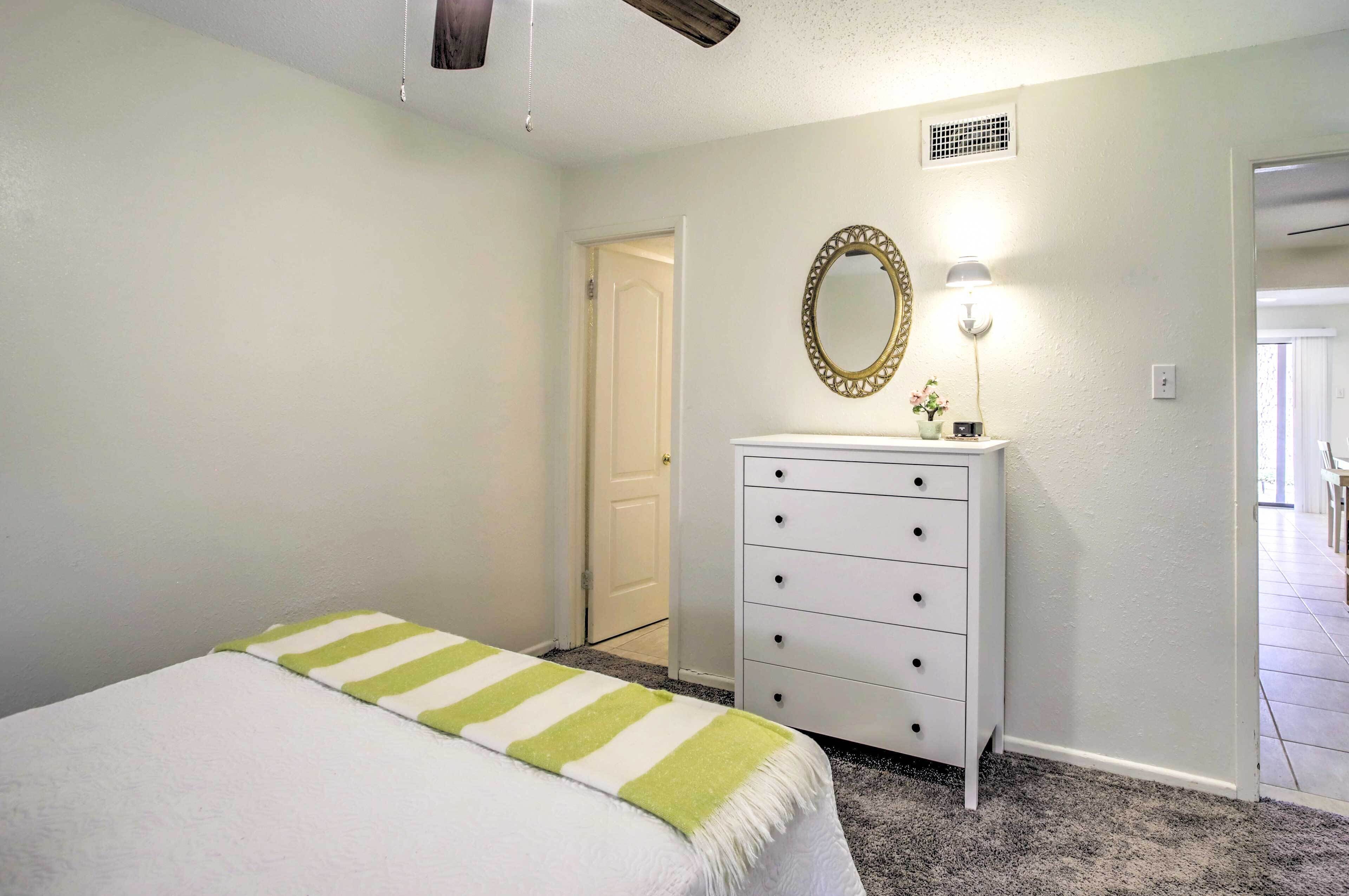Um quarto com cama, cômoda, espelho e luminária fixada na parede.