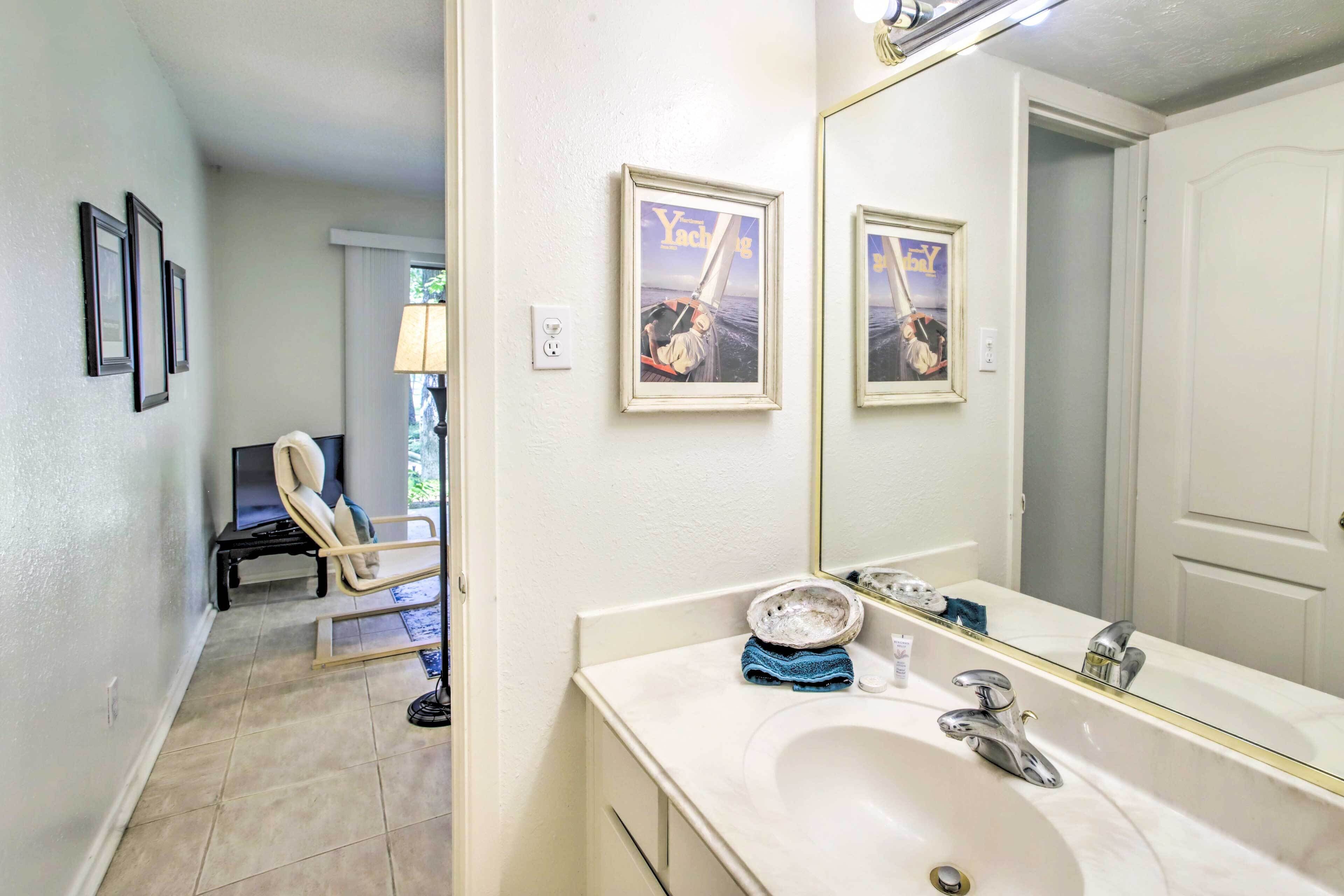 Et badeværelse med et stort spejl, en håndvask og billeder i rammer på væggen.